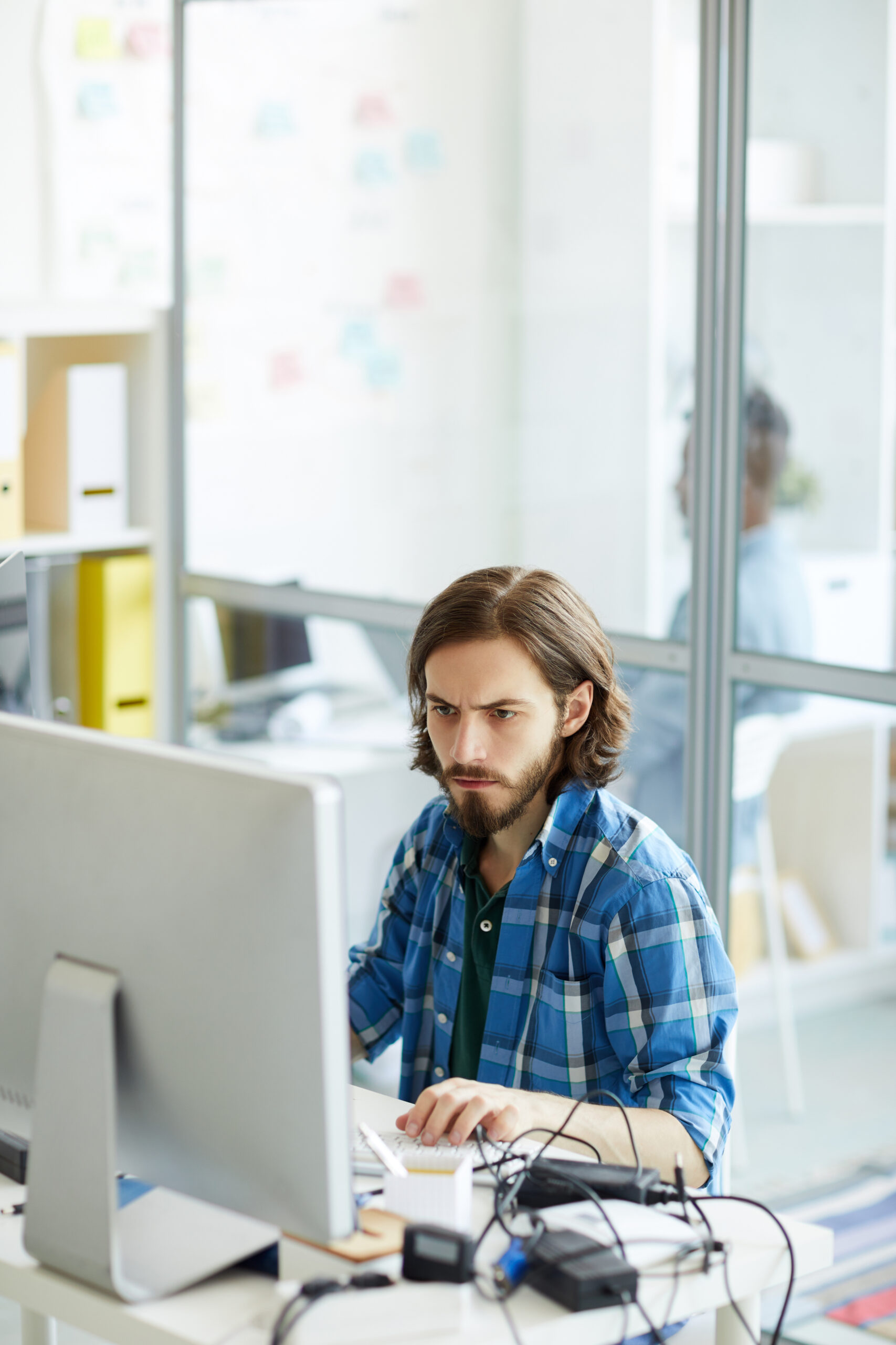 IT specialist focusing on computer problem Concentrated busy young IT specialist with beard and mustache focusing on computer problem and attentively examining data on computer in office