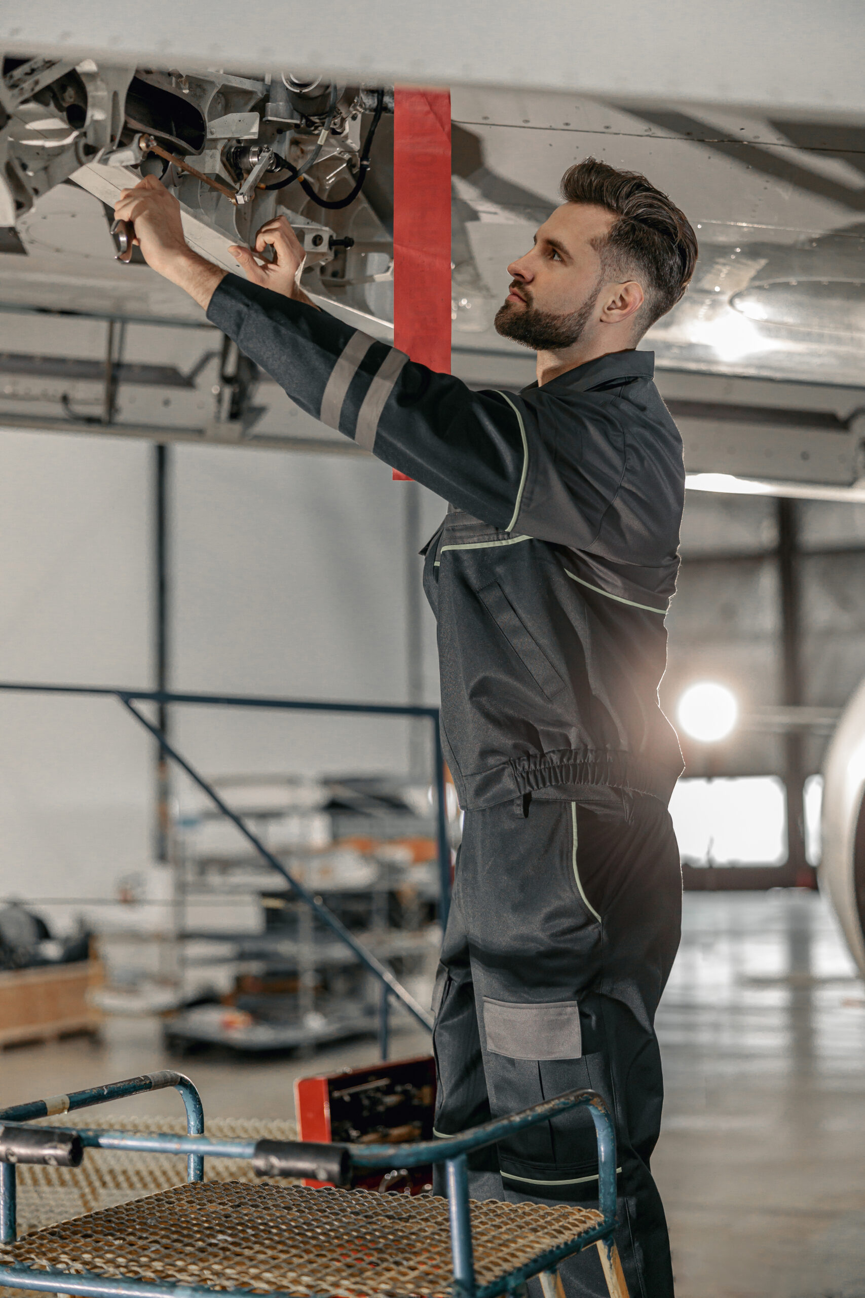 Male aviation mechanic repairing aircraft at repair station Bearded man maintenance technician tightening bolt with wrench while repairing airplane in hangar