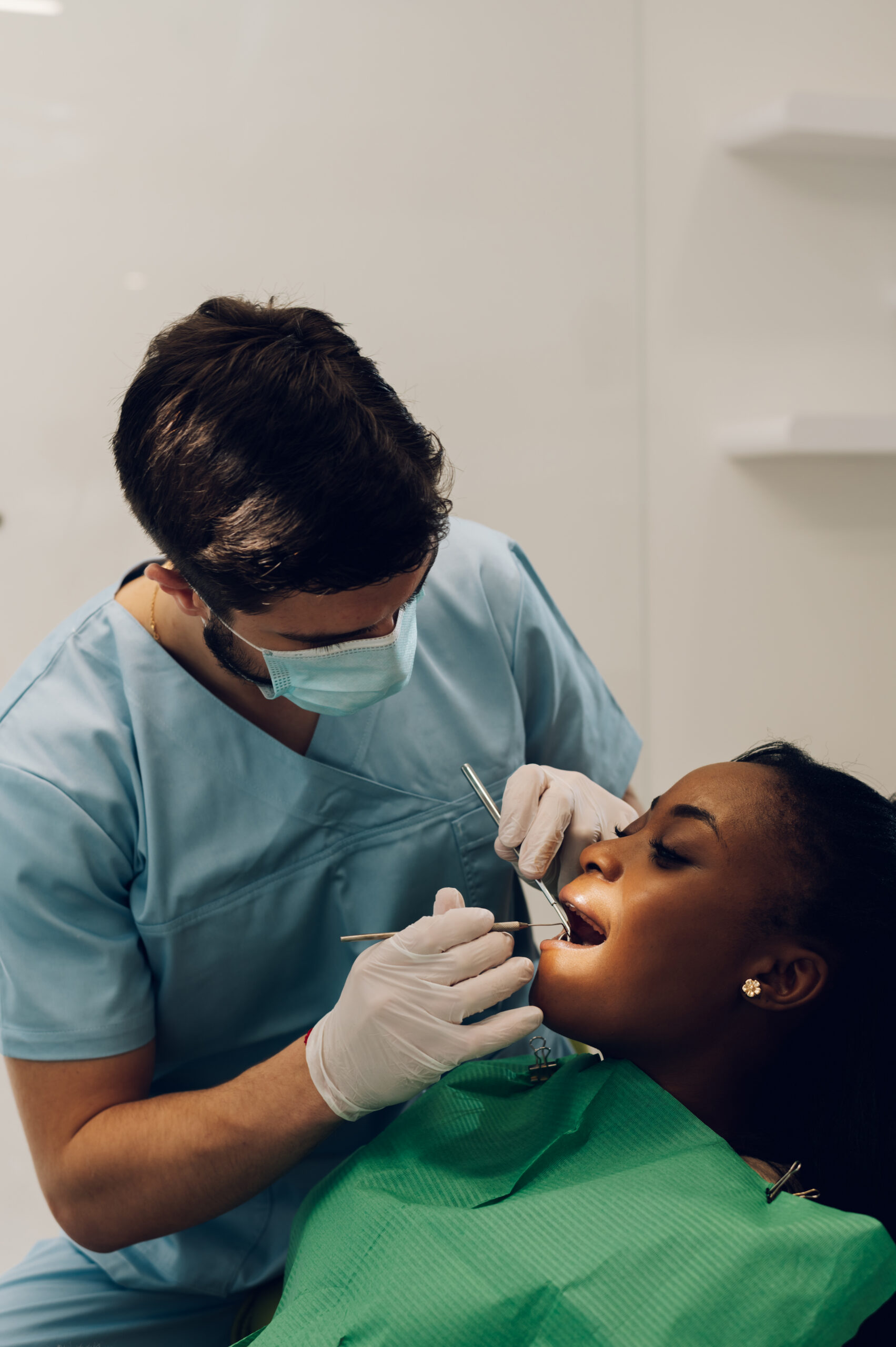 Young african american female patient with open mouth at dentist office. Black woman in dental clinic with male dentist fixing her teeth.